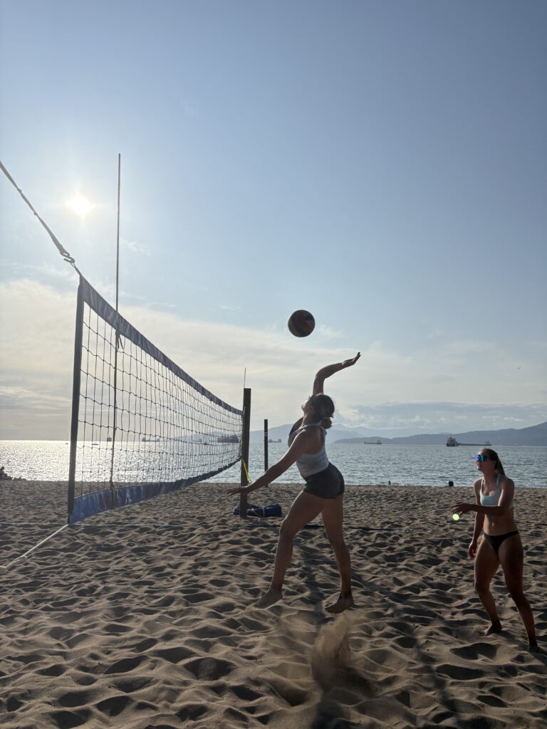 Beach volleyball player hitting a ball with the ocean and beach in the background at Kitsilano Beach.