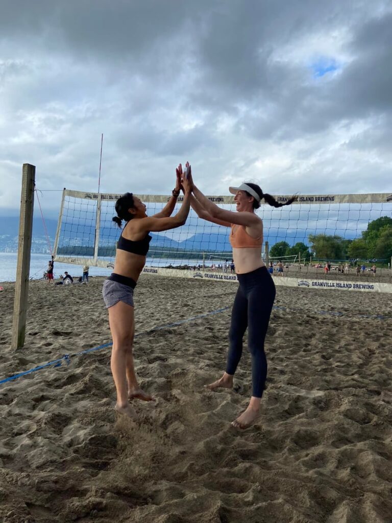 Beach volleyball teammates celebrating with a jumping high five on the sand court